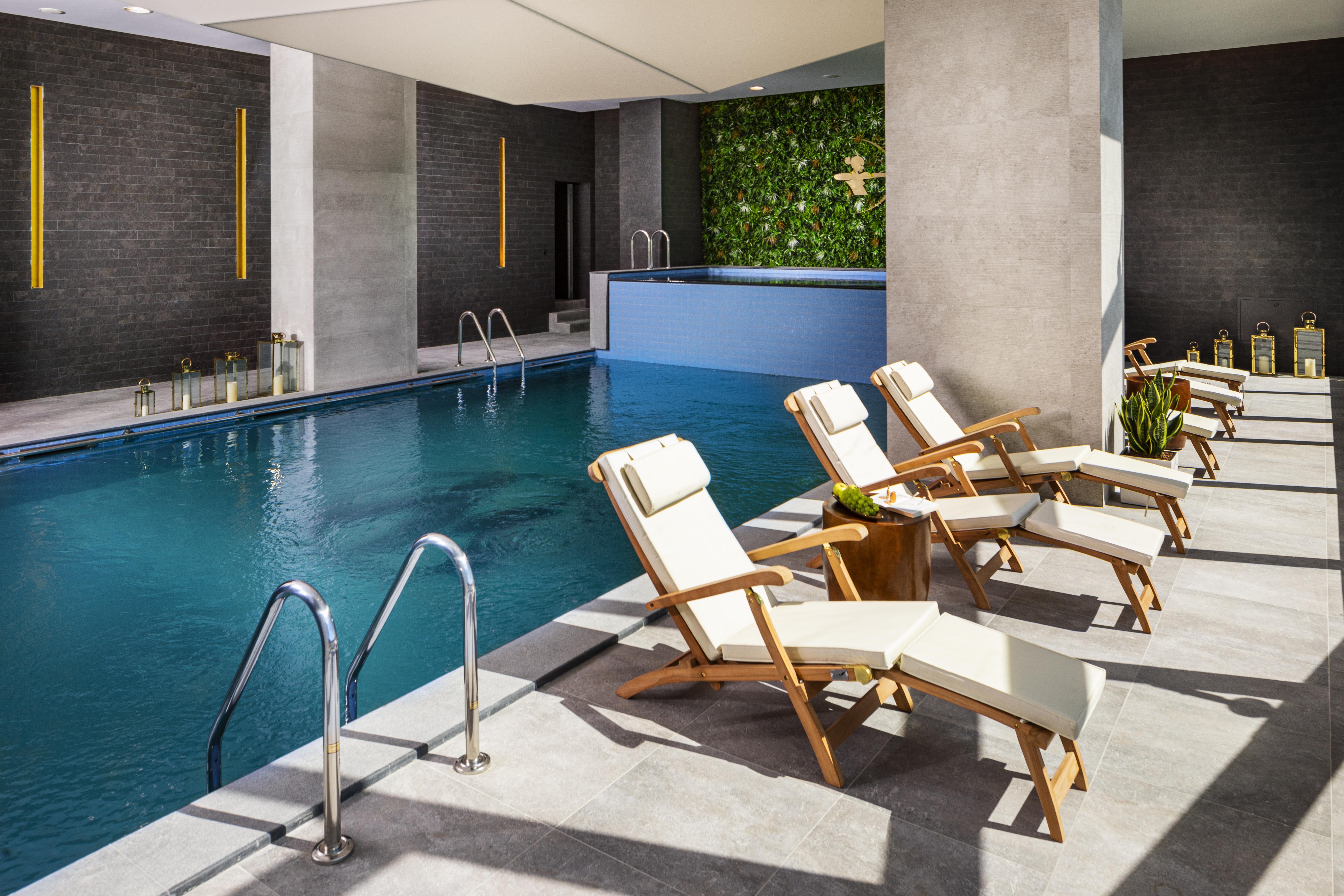 Grand Hotel Millennium Sofia Ngoại thất bức ảnh The photo shows a serene indoor swimming pool area. The pool is clear and inviting, with a blue water surface reflecting light. Along one side of the pool, there are several light-colored lounge chairs with white cushions, positioned for relaxation. 